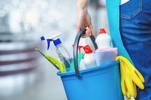 Hand holding bucket filled with dish detergent vinegar phynil bottles and other house cleaning stuff